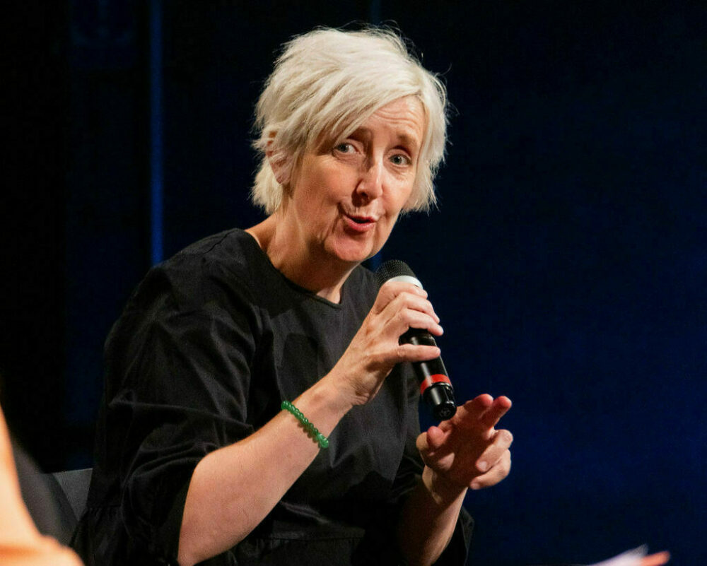 Actor Julie Hesmondhalgh wearing a black top speaking in to a microphone at the Youth Collective's The Art World Is Our World Festival at Contact Manchester, June 2023. Photo by Ronke Hart