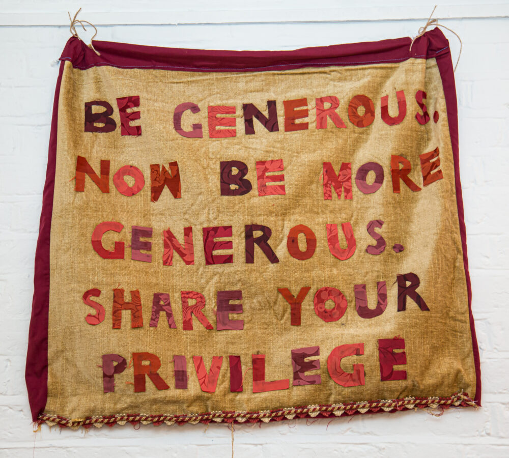 A banner made of material with letters on that reads 'Be generous. Now be more generous. Share your privilege'