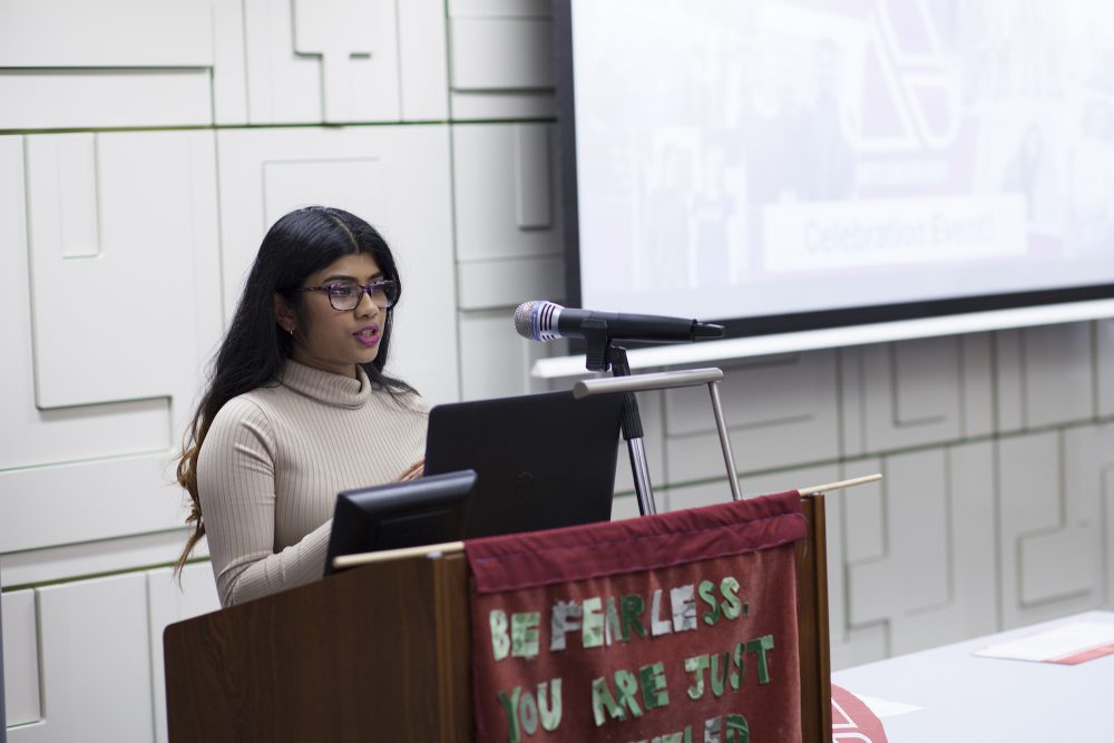 A young woman speaks from behind a podium into a microphone.