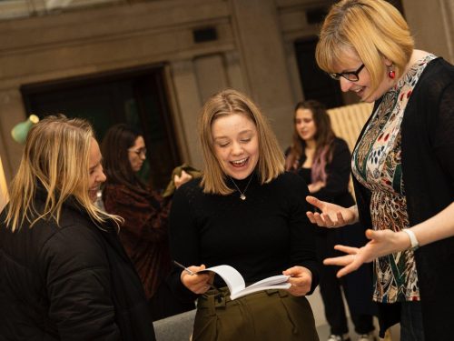 A young person shows a publication to two women stood either side of her.