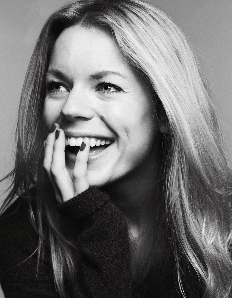 A black and white headshot of a white woman with long blonde hair laughing