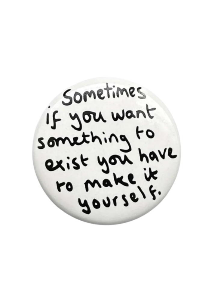 A white button badge with handwritten black text on reading 'Sometimes if you want something to exist you have to make it yourself'