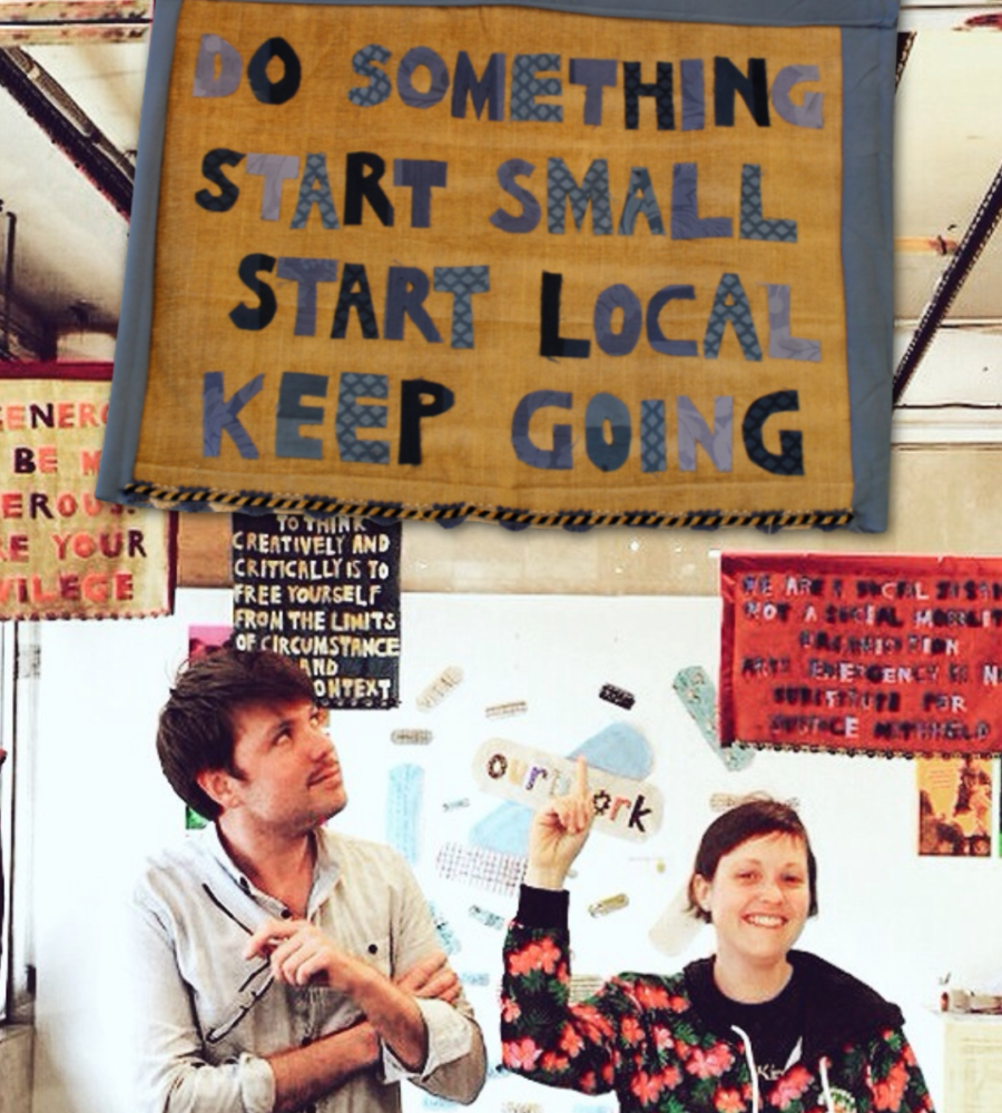 A male and a female in a room with several banners hanging from the ceiling. They are looking and pointing to one that reads 'Do something. Start small. Start local, keep going'