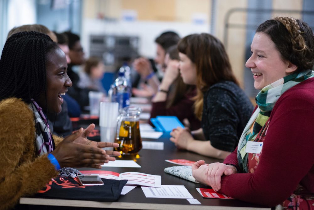 Smiling mentors and mentees sit across a table from each other.
