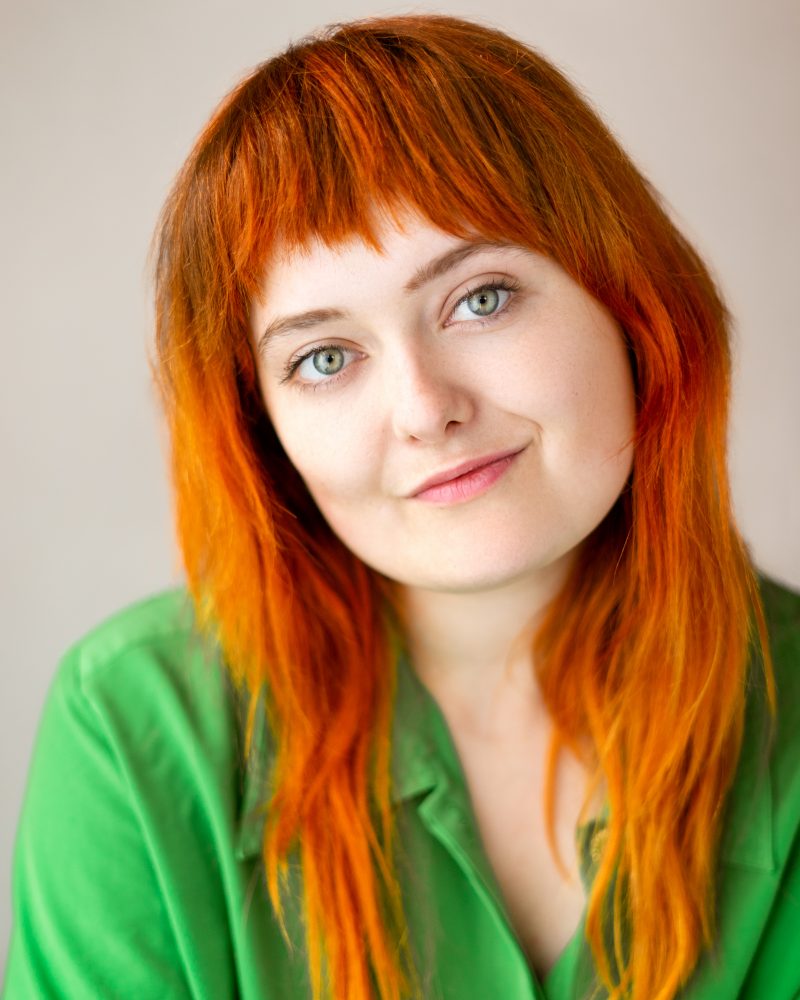 A head and shoulders portrait of a young woman with red hair and a green top