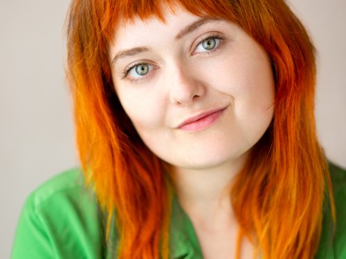 A head and shoulders portrait of a young woman with red hair and a green top
