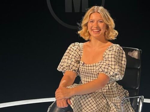 Female comedian Olga Koch sitting in a tv studio smiling and wearing a black and white dress