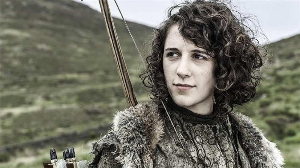 A still from a film in which a young woman wearing fur and carrying a bow and arrow is looking into the distance