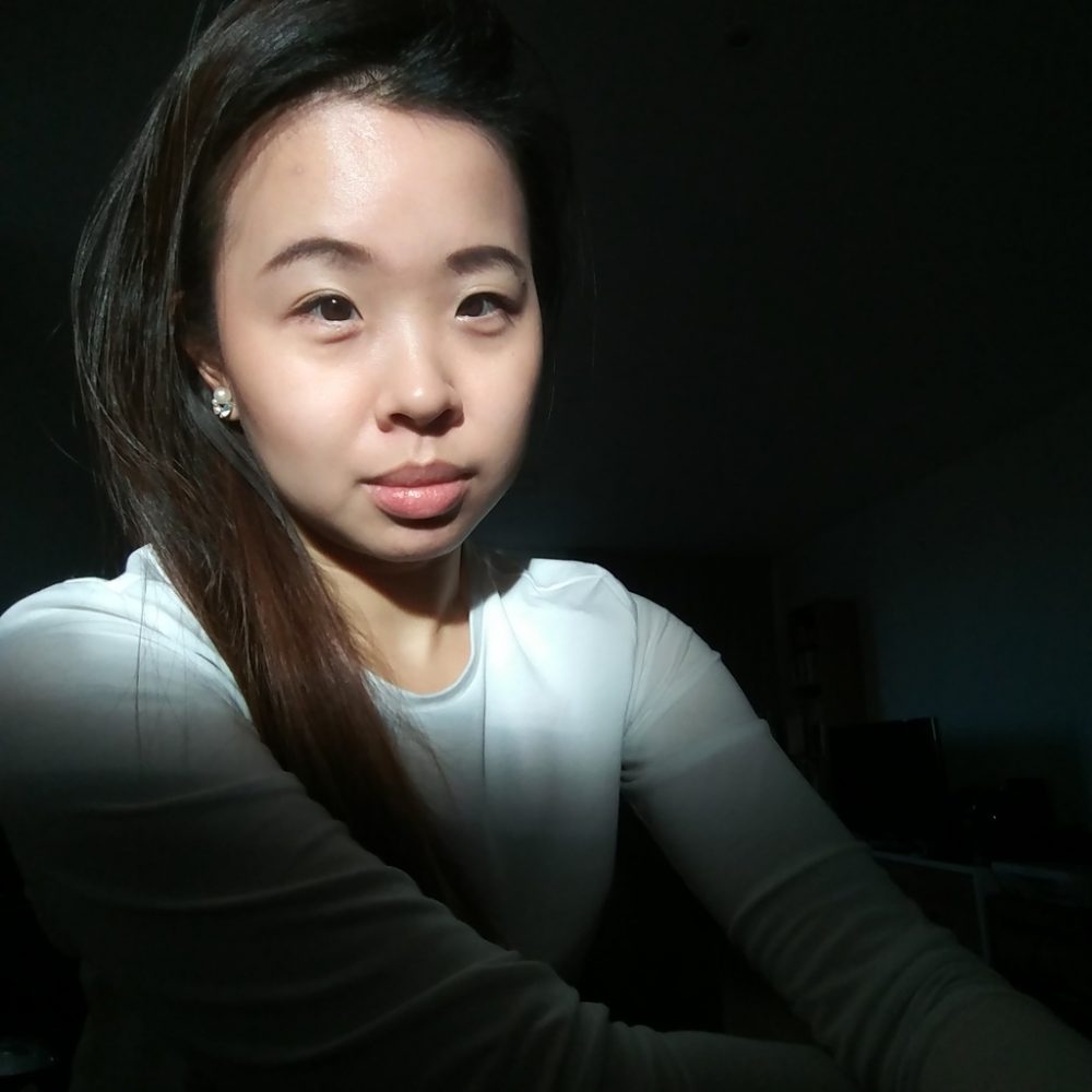 Jane Chan, an east Asian woman with long dark hair illuminated by sunlight against a dark background. She's wearing a white top and smiling slightly.