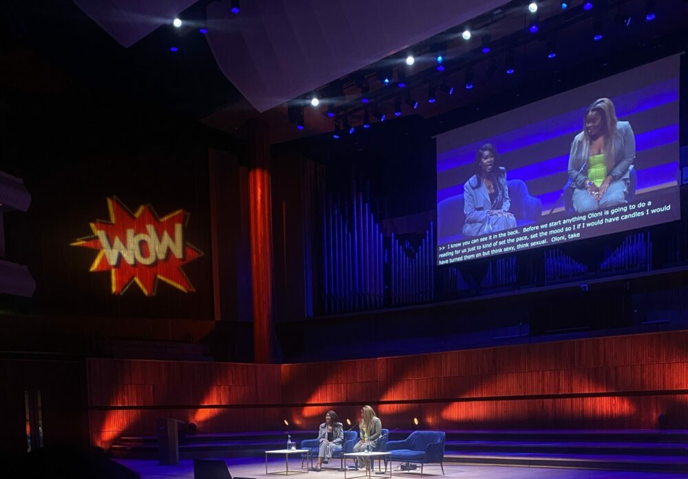 2 people on stage in discussion with a projection with the WOW logo on