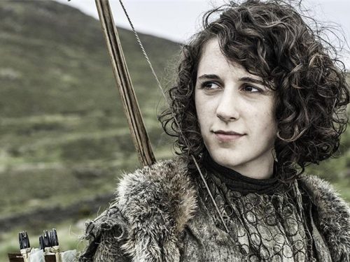 A still from a film in which a young woman wearing fur and carrying a bow and arrow is looking into the distance