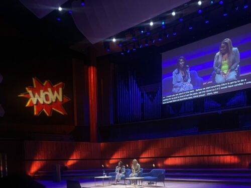 2 people on stage in discussion with a projection with the WOW logo on