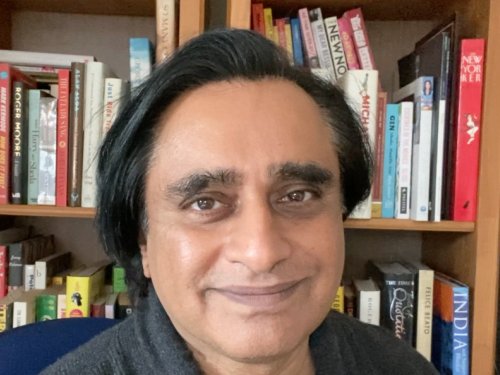 A man smiles in front of a full bookcase.