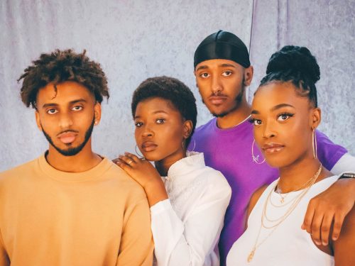 A group of two young Black men and two young black women, standing close together looking directly at the camera.
