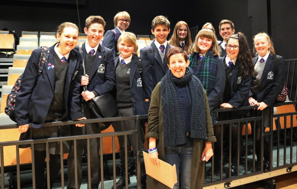 Julie Hesmondhalgh stands in front of a group of about ten school pupils wearing uniform