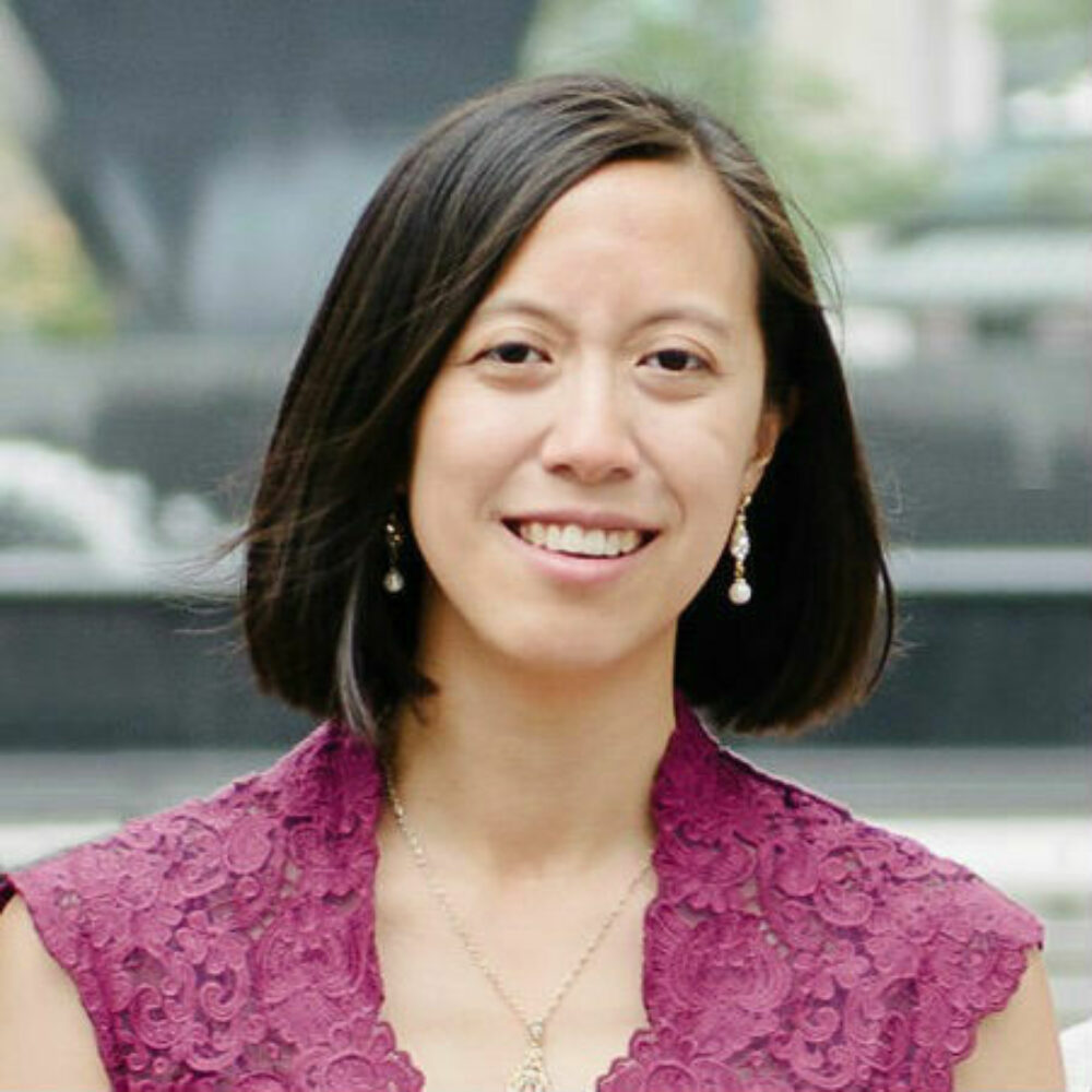 A person with shoulder length dark hair and wearing a pink sleeveless top smiling.