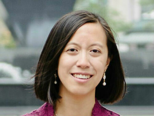 A person with shoulder length dark hair and wearing a pink sleeveless top smiling.