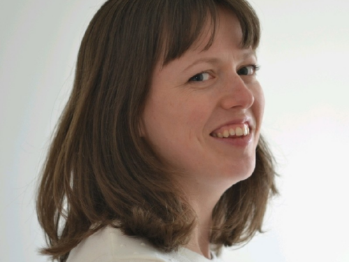 A head and shoulders photo of a woman with brown hair and white top, they are smiling