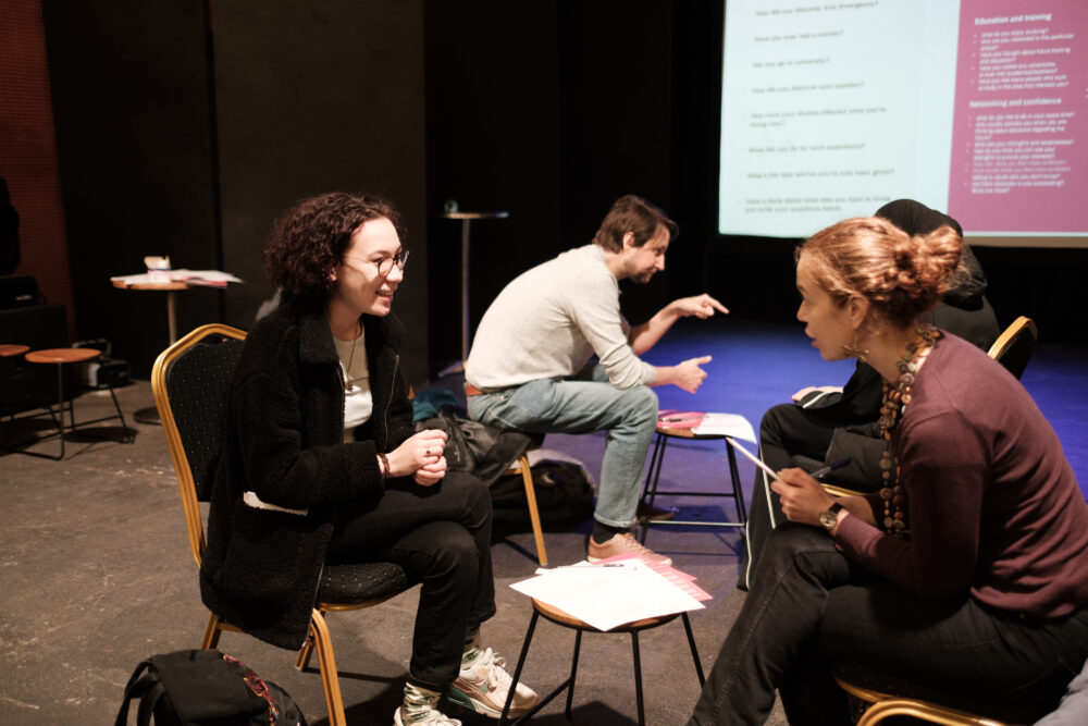 A person aged 18 sitting and speaking face to face with another person who is older than them.