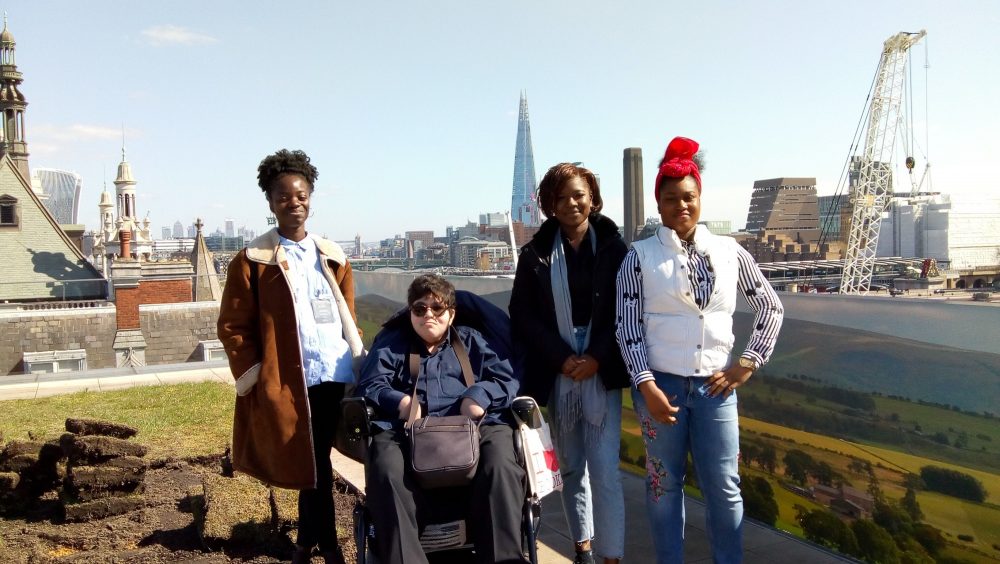 In front of a backdrop of the london skyline, four people smile at the camera