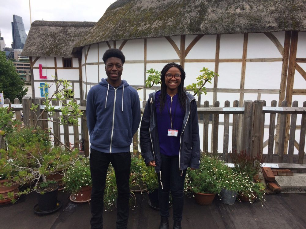 Two young people standing in front of potted plants in front of a round, white theatre