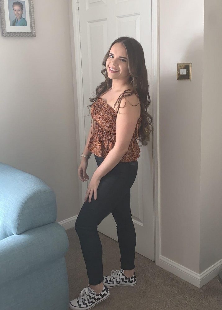 A young woman with long brown hair stands inside a house