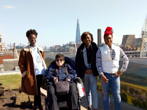 In front of a backdrop of the london skyline, four people smile at the camera